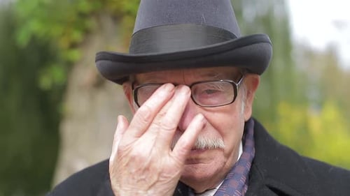 Senior Gentleman With Hat Wipes His Glasses