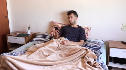 Mec fatigué utilisant un smartphone dans la chambre à coucher pour soulager l'ennui.