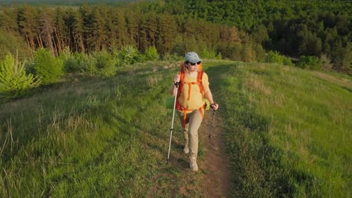 Young Woman Traveler with Backpack and Trekking Poles Climbing the Mountain