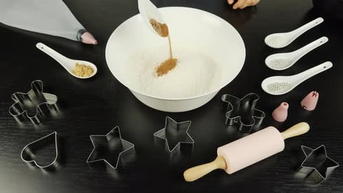 Hand is adding spices to flour in bowl, preparing gingerbread cookies for St. Valentine's Day