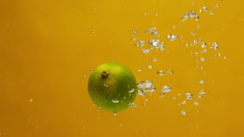 Closeup of Falling Limes Into the Water with Ice on Orange Background Making a Cocktail of Citrus