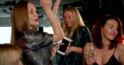 Viele Mädchen in leuchtend glänzenden Kleidern tanzen, hängen ab und haben Spaß auf einer Party in einem Bar-Club.
Sie