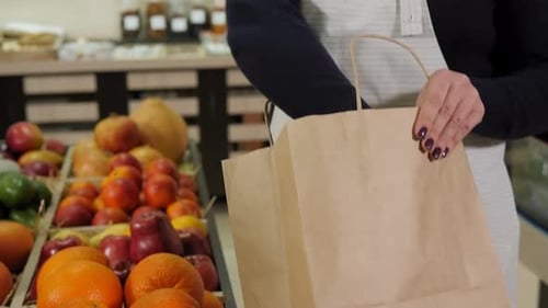 Primer plano de una vendedora con un delantal poniendo naranjas en una bolsa ecológica