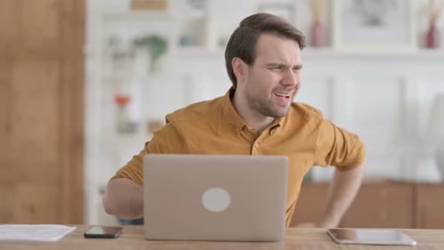 Young Man having Back Pain while using Laptop in Office