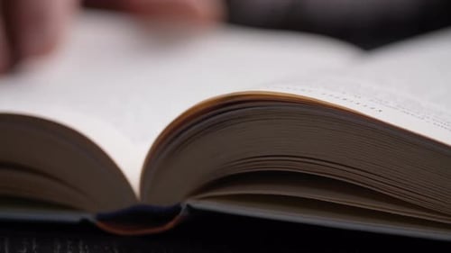 Unrecognizable person reading a book. Hand Turning Pages of a Book, close up.