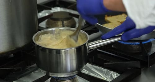 Professional kitchen close up of chef hands wearing gloves stirring mushroom cream sauce in stainles