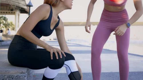 Young Asian Woman Helping Friend Suffering From Pain and Discomfort with Ankle Sprain During Running