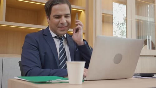 Smiling Man Working at Desk on Laptop and Cellphone