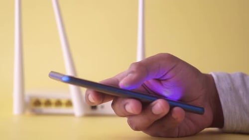 Hand Using Smartphone Near WiFi Router