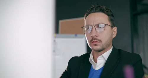 Closeup Portrait of a Businessman Wearing Glasses Sitting in His Office in Front of a Monitor