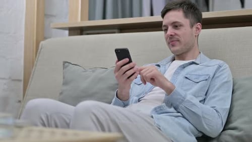 Man Relaxing on Couch Using Smartphone