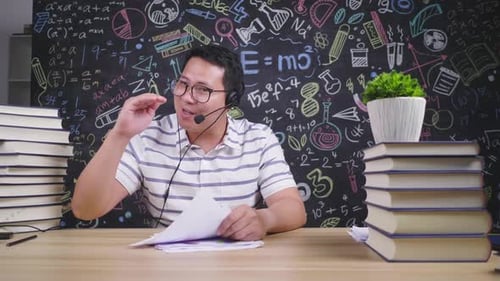 Front view of Asian man having a meeting online on laptop, taking note and using wireless microphone
