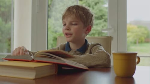 School Kid Reading Paper Book Sitting Alone at the Table at Home