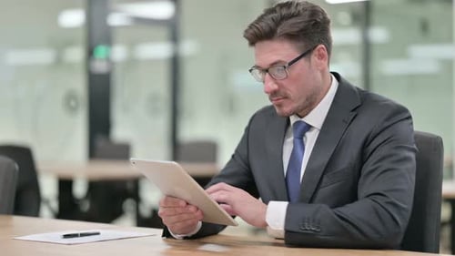 Serious Professional Middle Aged Businessman Using Tablet in Office