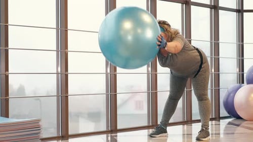 Curvy Girl Exercising with Fitness Ball in Gym