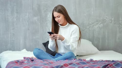 Woman Using Smartphone Sitting on Bed Indoors