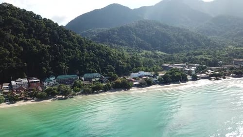 The green hills of the island are covered with palm trees, the sky is cloudy