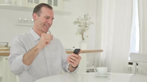 Man Celebrates Good News on Phone at Home