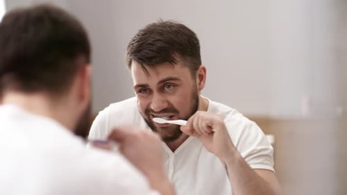 Caucasian Man Brushing Teeth and Looking in Mirror
