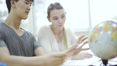 Teenage boy and girl studying globe in classroom