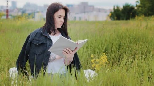 Intelligente kaukasische Frau sitzt draußen auf Rasen liest Buch Literatur Psychologie Bestseller