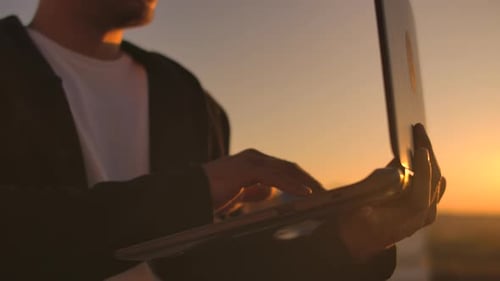 Person Typing on Laptop at Golden Sunset