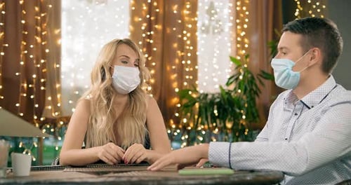Couple with Masks Reads Menus at Restaurant Table