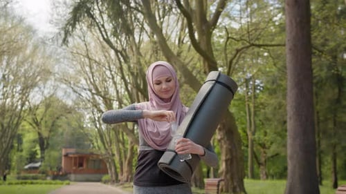 Side View of Pretty Young Woman in Hijab and Activewear Drinking Water From