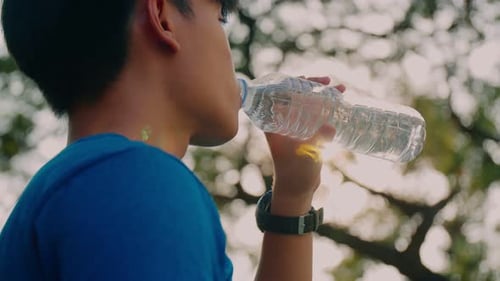 Man caucasian athlete drinks water after running at the park.
