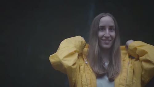 Porträt eines kaukasischen Reisemädchens in gelbem Regenmantel in der Nähe eines Wasserfalls im Wald