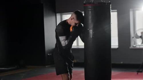 Athletic Young Man Boxer Hitting the Punching Bag in the Gym