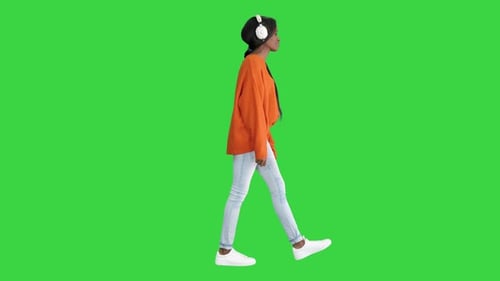 Smiling African American Woman with Headphones Walking Listening To the Music on a Green Screen