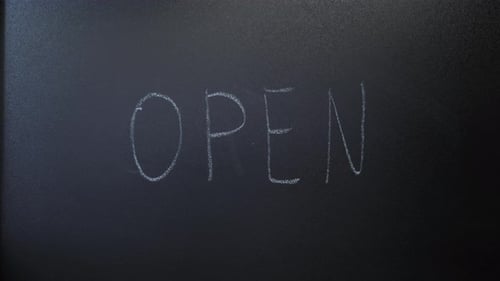 Male hand writing word Open on chalkboard.