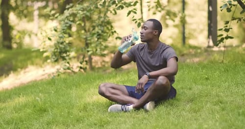 Man Drinking Water Bottle After Exercise in Park