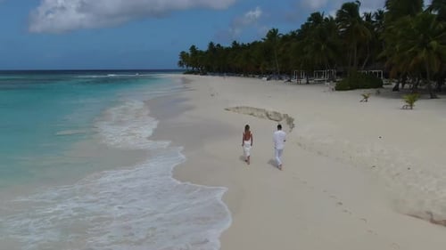 Aerial View of Two Young People in White Clothes Walking on a Tropical Beach