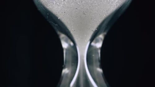 Glowing Sand Pours Down in Traditional Hourglass on Black