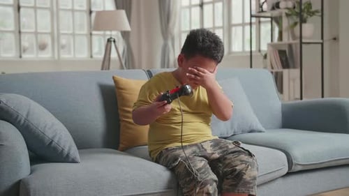 Ernster Junge spielt Videospiel mit Joystick im Wohnzimmer und fühlt sich unglücklich