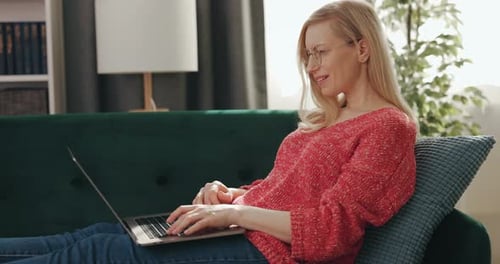 Woman Working on Laptop While Relaxing on Sofa