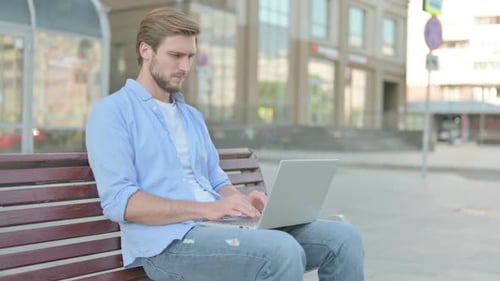 Young Man Using Laptop on Bench Outdoors