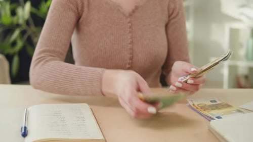 Woman Counting Euros and Writing in Notebook