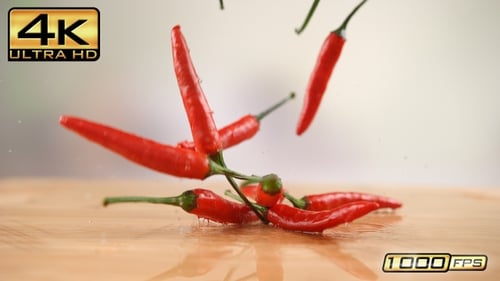 Red chili peppers falling on wooden board