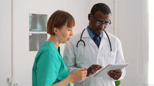 Male Doctor Using Tablet and Talking to Female Colleague at Medical Clinic Spbas