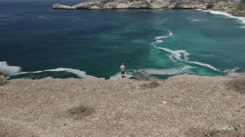 Man on Top of Cliff Controlling Drone in an Aerial Shot Overlooking Lombok