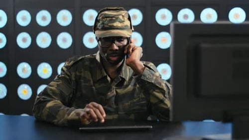 Man in Camouflage Uniform Talking on Phone at Computer