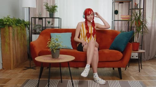 Happy Relaxed Girl in Wireless Headphones Dancing Listening Favorite Rock n Roll Music on Home Couch