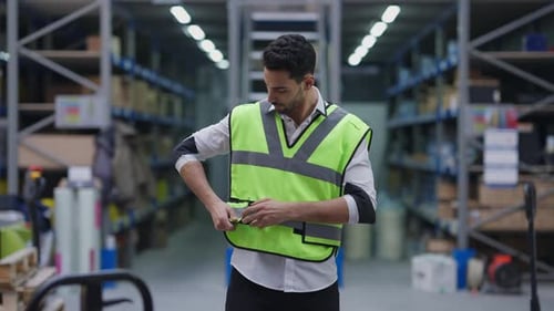 Apuesto hombre barbudo del Medio Oriente atando velcro en el chaleco de pie en un almacén industrial