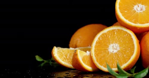 Pieces of Ripe Orange with Leaves Falling Drops of Water.