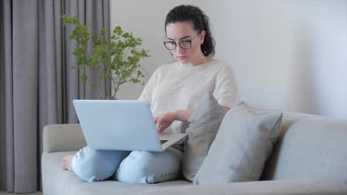 Woman Works on Laptop at Home on Sofa