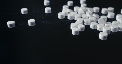 Pills Falling onto Dark Reflective Surface