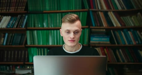 A Young Guy Is Sitting in the Library and Working on a Laptop . A Beautiful Girl Is Standing in Blue